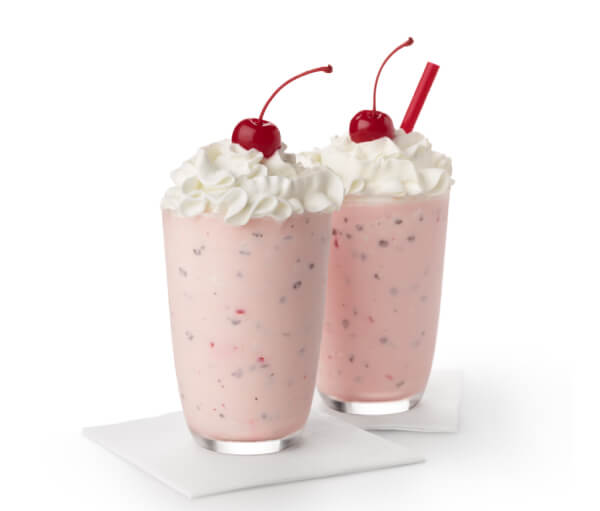 Two pink milkshakes with whipped cream and a cherry on top