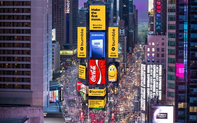 A view of Times Square. Six of the nine screens on 2 TImes Square behind the Red Steps have yellow ads for Bumble on them.