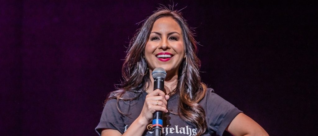 Anjelah Johnson on stage holding a microphone