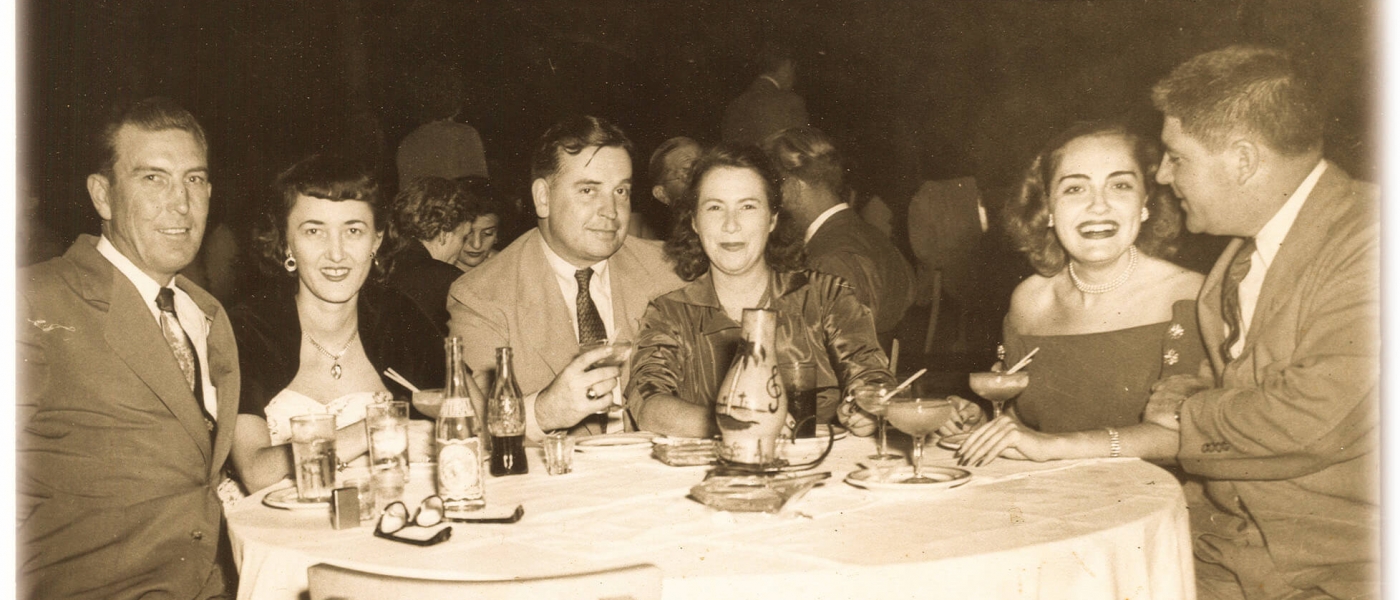 Sepia-toned historical photo of three couples at a dinner table