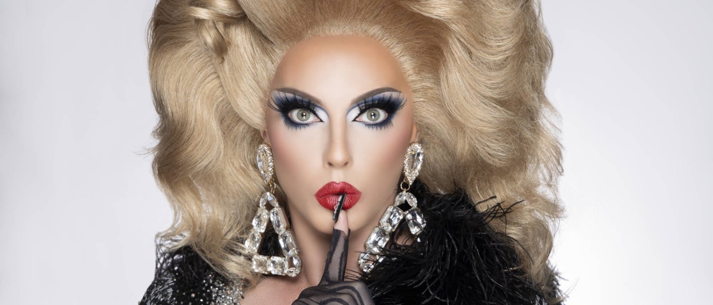 Alyssa Edwards in full glam makeup and hair, holding a finger to her lips