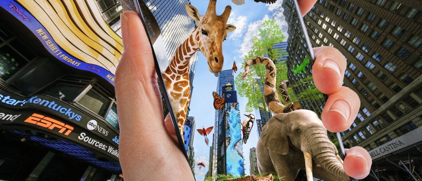 A hand holding up a phone in Times Square. The phone screen shows the same view of Times Square, but with animals like a giraffe, an elephant, a cheetah, and more