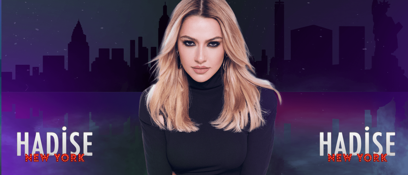 Hadise looking at the camera in a black turtleneck. A silhouette of the NYC skyline is behind her.