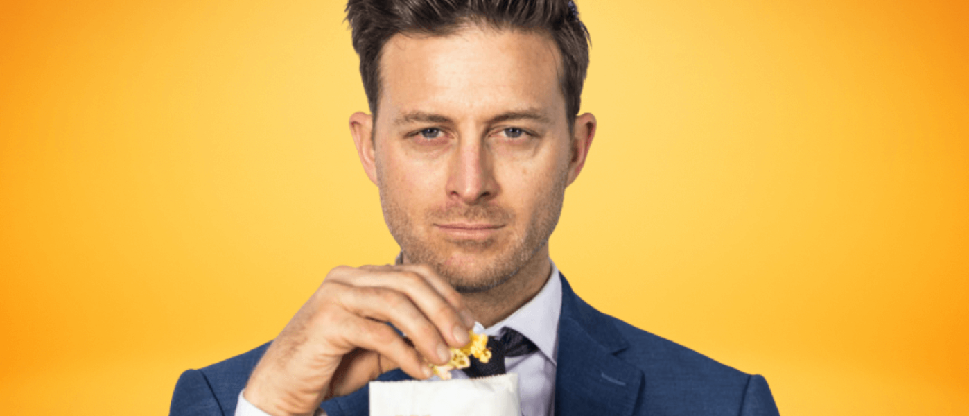 K-von eating popcorn out of a bag while wearing a suit in front of a yellow background