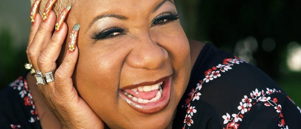 Luenell resting her head on her hand and smiling