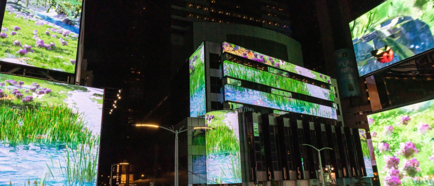 eye-land by KESH on the screens of Times Square, showing flowers, grass, and a lake