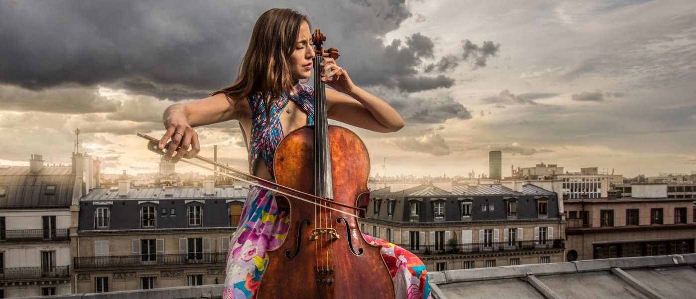 Camilla Thomas in a floral dress playing cello on a rooftop
