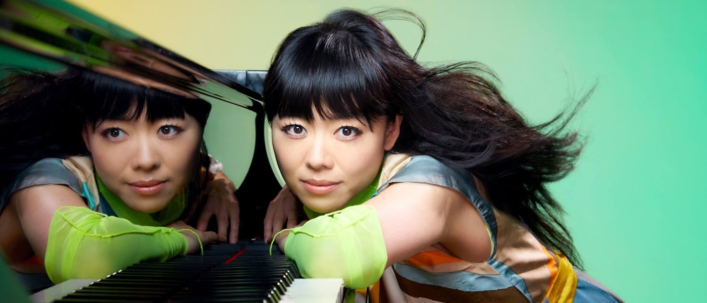 Hiromi leaning with her elbows on the keys of a piano