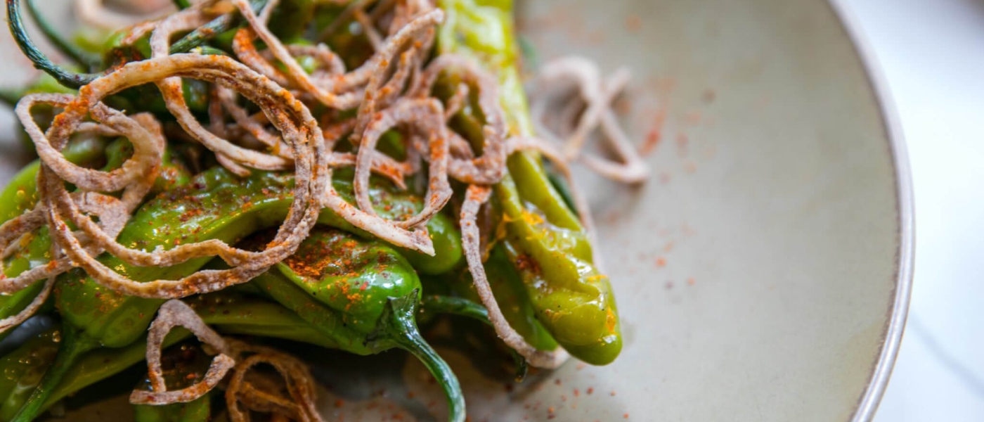 Blistered peppers topped with crispy thinly-sliced onions and a reddish seasoning mix on a plate