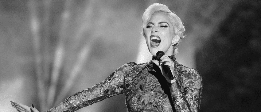 A black and white photo of Lady Gaga singing in a long-sleeved lace dress