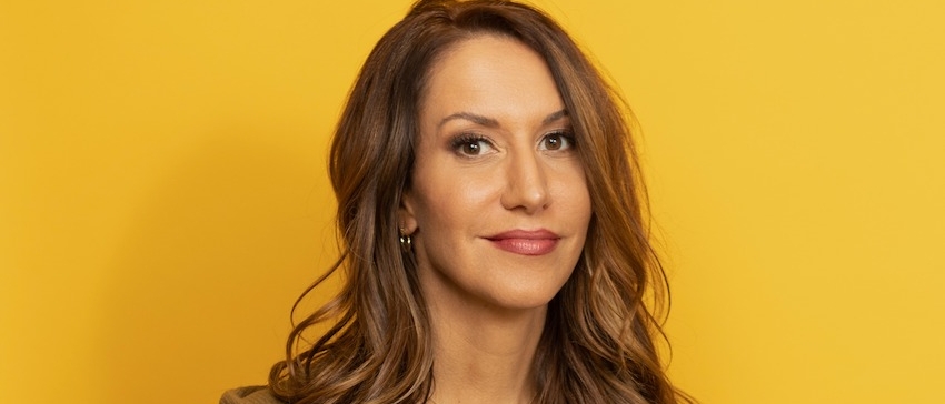 Rachel Feinstein smiling ambivalently in front of a yellow background