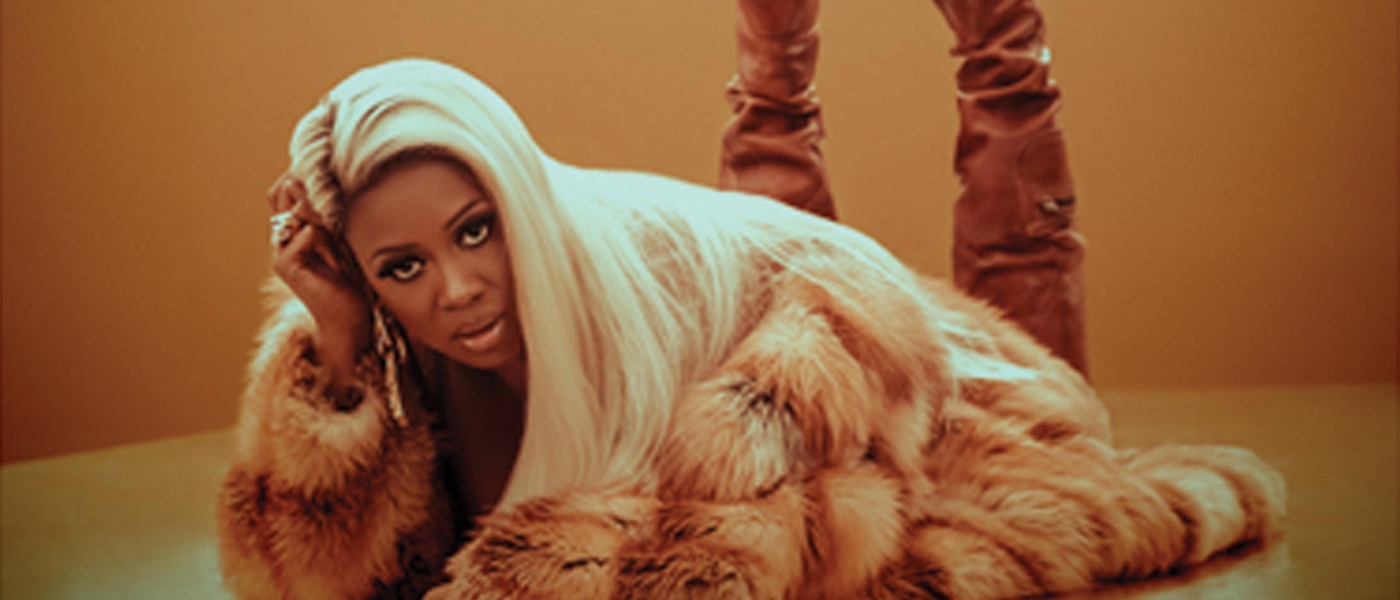 Remy Ma lying on her stomach in a fur coat and boots