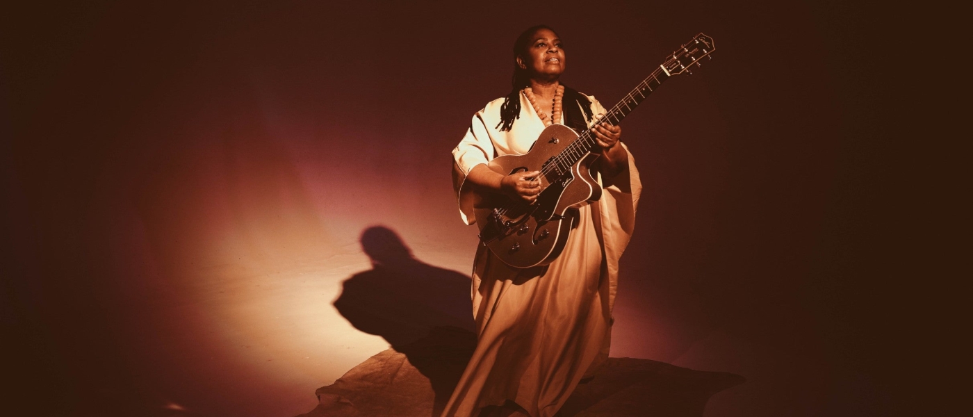 Ruthie Foster wearing long draping clothing and playing a guitar