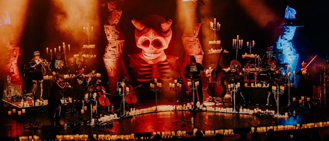Classical musicians wearing skeleton costumes on a stage filled with candles and candelabras 