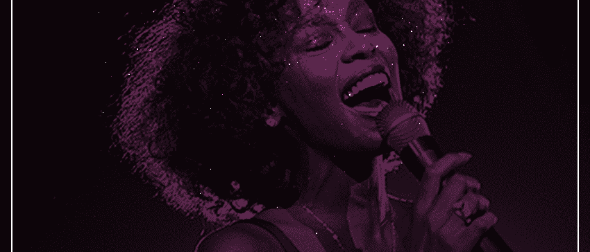 A black and purple image of Whitney Houstin singing into a microphone