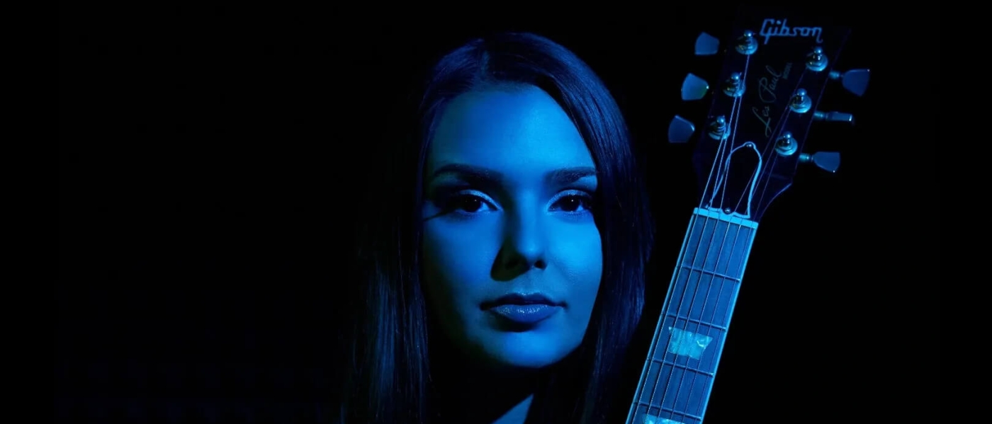 A blue-toned photo of Ally Venable holding a guitar