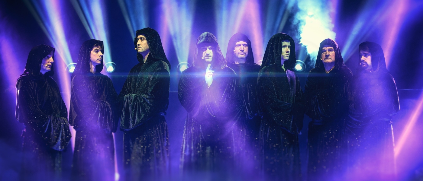 The members of Gregorian wearing black hooded robes on stage