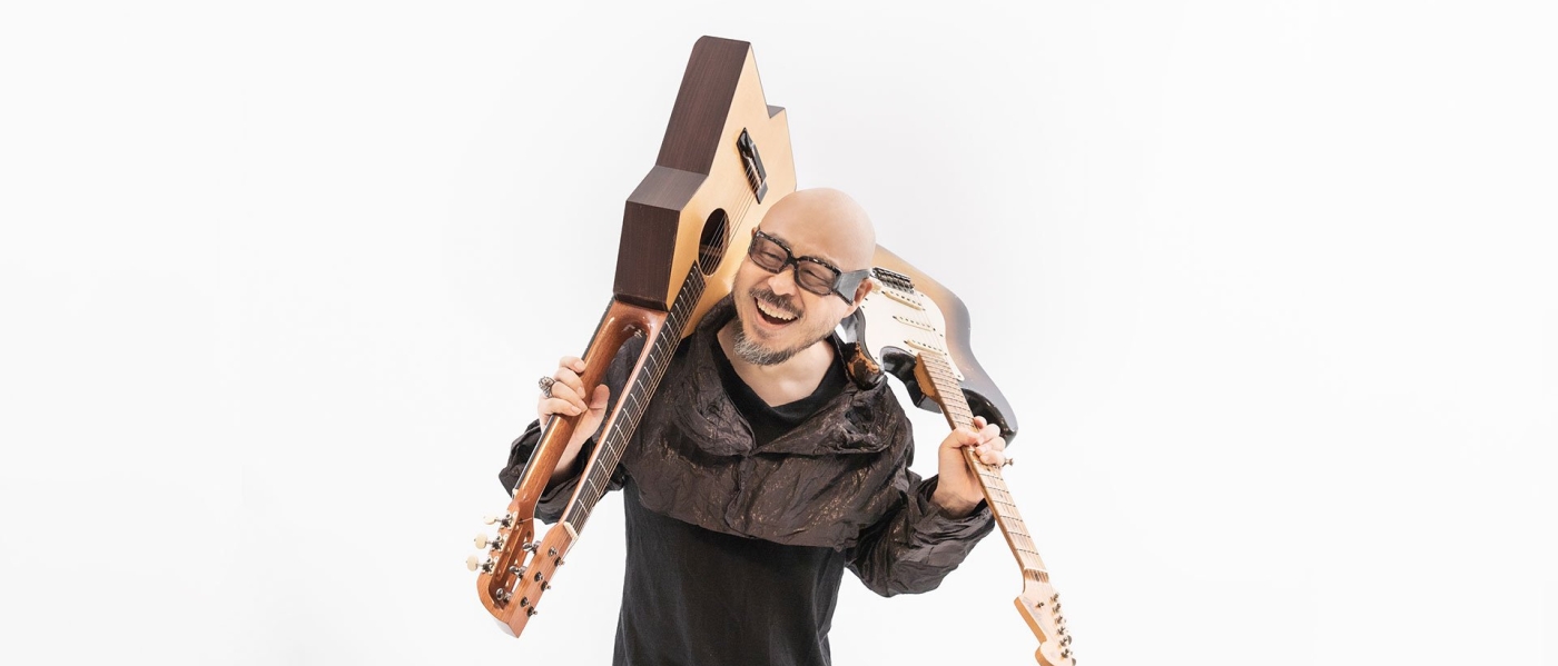 Lee Byeong-Woo, a middle-aged Korean man, hoisting an electric guitar over one shoulder and an angular double-sided guitar over the other