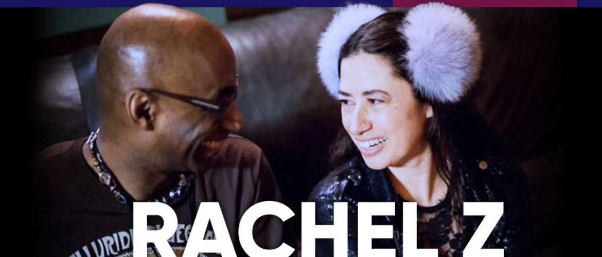 Rachel Z and Omar Hakim sitting on a couch and smiling at each other