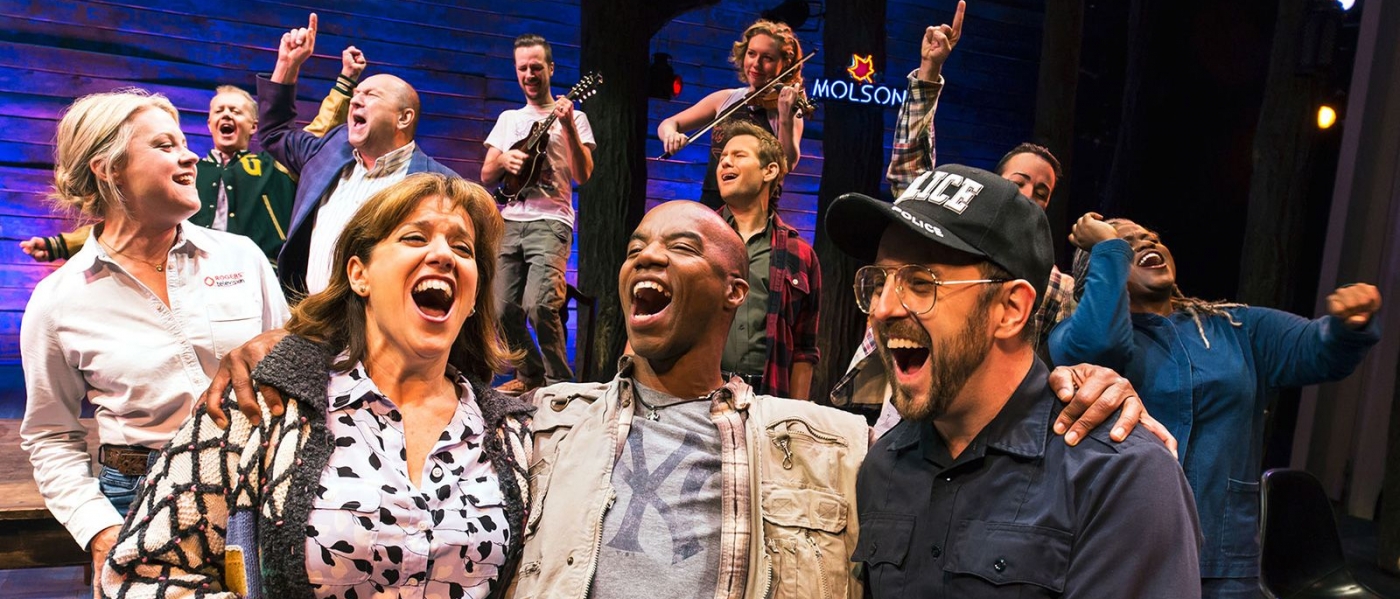 A production photo of Come From Away with the cast close together and singing