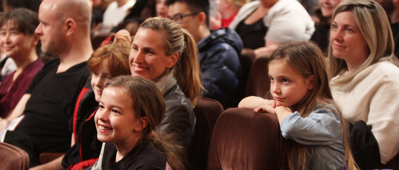 Kids and parents in the audience of a show, smiling up at the stage