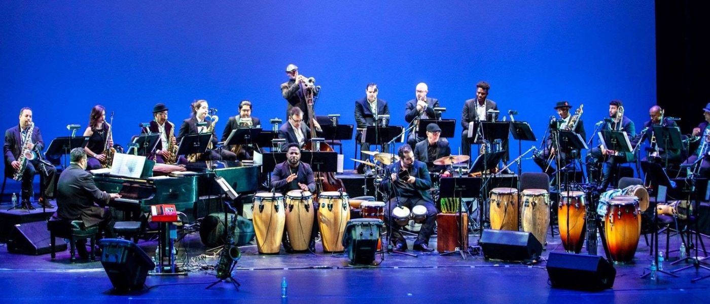 An 18-piece orchestra with a variety of drums on stage