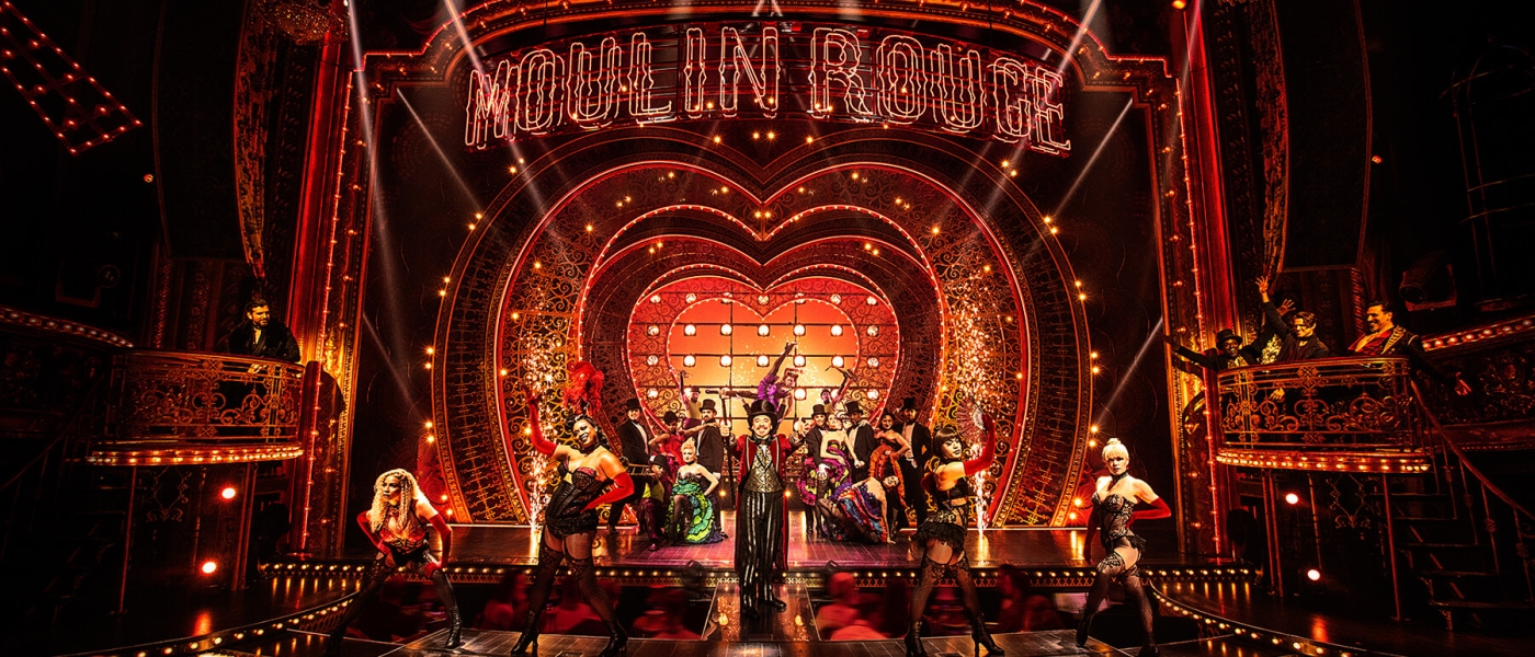 The cast of Moulin Rouge! The Musical on stage with the iconic heart-shaped backdrop
