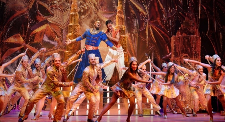 Michael James Scott as the Genie and Michael Maliakel as Aladdin in Aladdin on Broadway, standing in a set designed to look like a cave full of gold, with ensemble dancers in gold