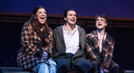 Lindsay Mendez (Mary Flynn), Jonathan Groff (Franklin Shepard) & Daniel Radcliffe (Charley Kringas) in MERRILY WE ROLL ALONG. They are seated on a bench and singing, looking happy.