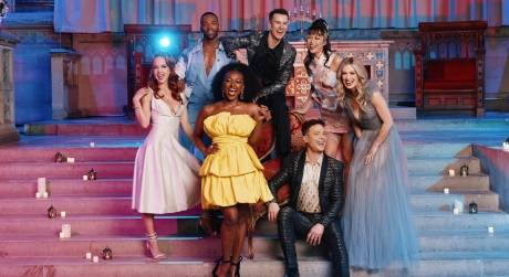 The cast of Once Upon a One More Time, wearing formal outfits in a variety of colors and posing on a set of steps in blue and pink lighting