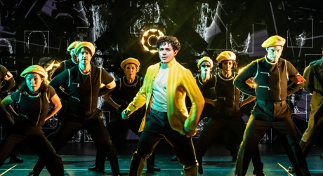 Ali Louis Bourzgui on stage as Tommy in The Who's Tommy, wearing a yellow jacket with background dancers in matching yellow berets