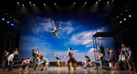 The cast of Water for Elephants on stage during a scene of the circus members rehearsing, with one woman flying through the air in the splits